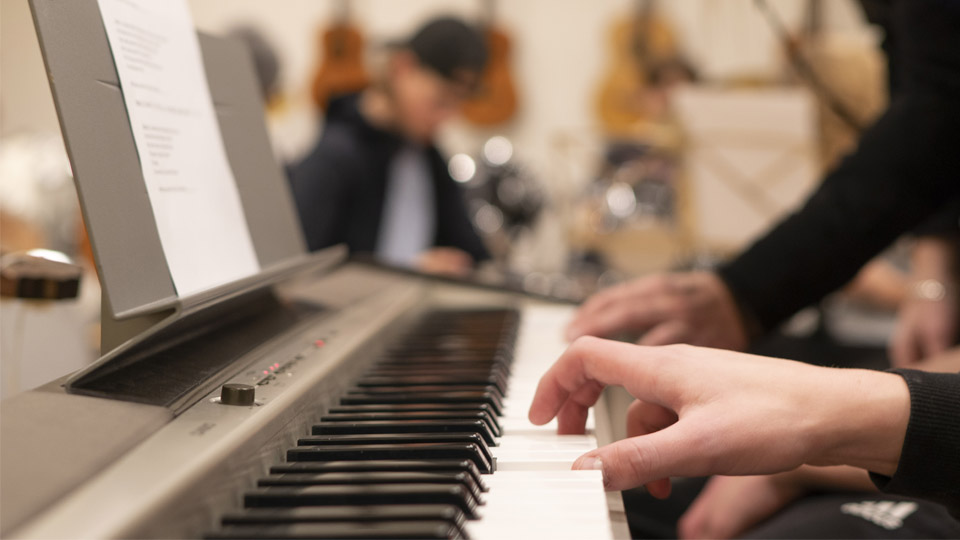 Närbild på händer som spelar piano och andra som spelar instrument i bakgrunden.