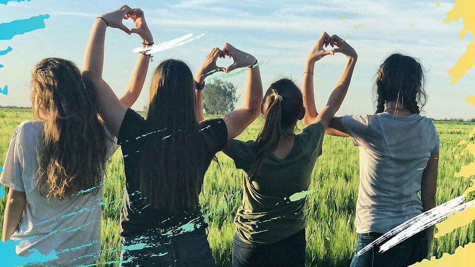Fyra tonåringar som står bredvid varandra på ett grönt fält. De använder varandras händer för att göra hjärtsymboler. Bilden ger en känsla av kärlek och gemenskap.